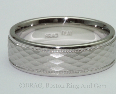 Men's platinum wedding ring with diamond shaped pattern and mill grain edge details.